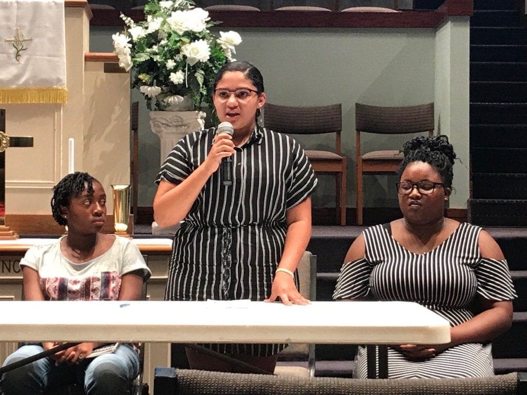 female student in vertical striped clothing speaking into microphone.