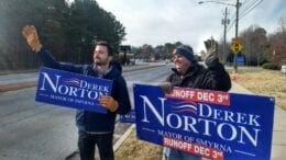 Two men waving Derek Norton signs on Spring Road in article Derek Norton wins