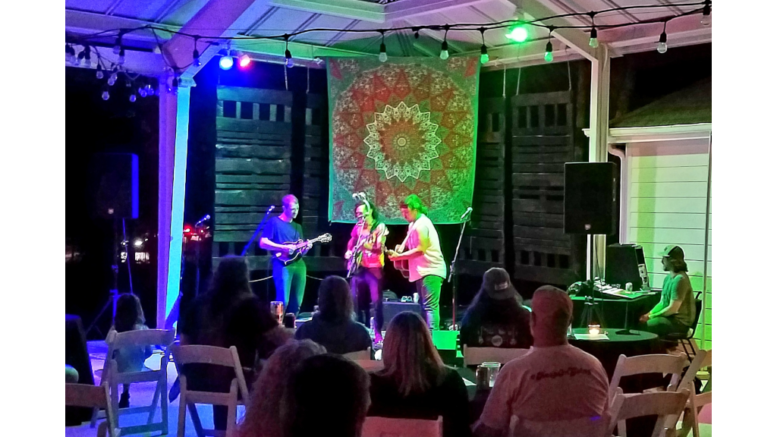 Three musicians on a small stage: mandolin, banjo and guitar