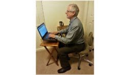 Larry Johnson, the editor and publisher of the Cobb County Courier seated in an office chair in front of a small table with a laptop in article about Cobb County Courier Meet the Editor