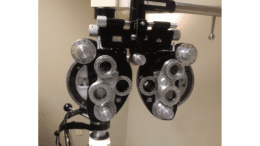 Captured inside an exam room inside an ophthalmologist’s office during a patient examination, this photograph depicts an optometric instrument used by the eye care specialist when performing eye examinations. Known as a phoropter, this device contains an array of lenses that are used in combination when testing a patient’s eyesight.
