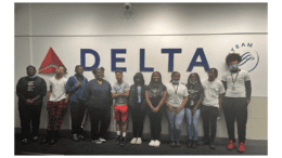 11 teens in front of a large DELTA Airlines sign