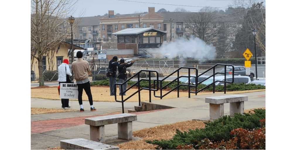 Two Black men dressed as Union Civil War soldiers fire muskets