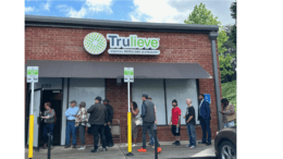 A group of people line up at a brick building with the sign Truelieve Medical Marijuana Dispensary