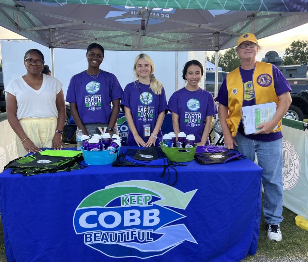 A diverse group of people at a Keep Cobb Beautiful table, smiling