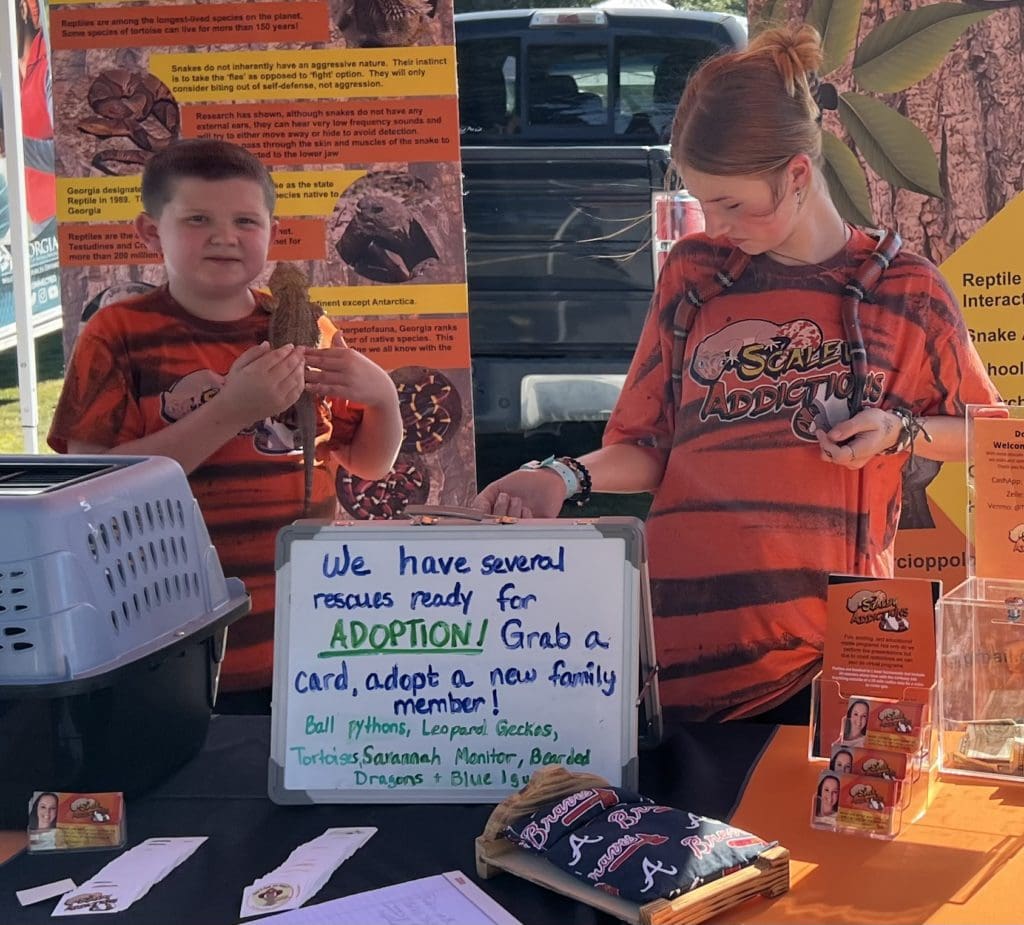 a rescue reptile table with two young people, one with a snake another with an iguana