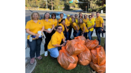 A large group of members of the Atlanta Latino Lions Club standing and kneeling around bags of trash they've collected along Windy Hill Road