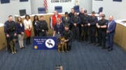 Cobb commissioners and police officials along with three dogs gather around sign stating "JoAnn K Birrell Police K9 Annex"