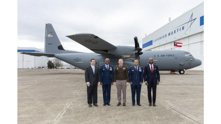 Five men in suits and military uniforms stand in front of a C-130J-30, a large gray turboprop aircraft
