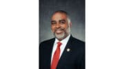 BOC District 2 candidate Erick Allen, upper body shot, smiling, neatly trimmed beard, wearing a dark jacket and red tie