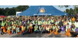 A large group of cleanup volunteers with yellow safety vests and orange bags