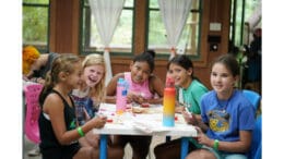 Several girls sit at a table with crafts in the Camp Timber Ridge dining hall